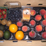 CSA Box with peaches, oranges, avocados, kiwis, strawberries, blueberries, and granola