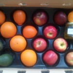 CSA Box filled with apples, oranges, tangelos, avocados, and a jar of olive oil.