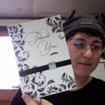Kimi holding up an on ornate thank you card with leaflike embellishments.