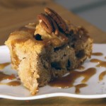 A square slice of apple cake topped with a toasted pecan and drizzled with a glaze.